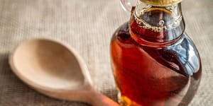 A jar of maple syrup and a wooden spoon on a table