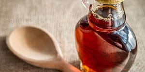 A jar of maple syrup and a wooden spoon on a table